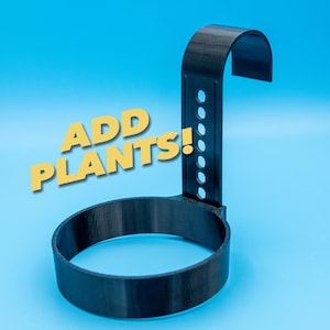 May include: Black plant holder with a circular base and a curved top, designed for hanging. The holder has a vertical support with several holes. The text "ADD PLANTS!" is displayed in yellow.