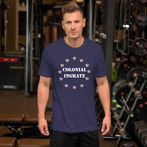 May include: A navy blue t-shirt with a white graphic print of stars and the text "Colonial Ingrate".