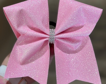 Puede incluir: Un gran lazo de animadora rosa brillante con un centro de diamantes de imitación. El lazo está hecho de un material brillante y está unido a una banda elástica negra. El lazo es de color rosa vibrante, ideal para animadoras o baile.