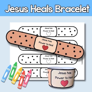 May include: A craft project featuring a bandage-shaped bracelet design with the text "Jesus Heals Bracelet." The design includes a bandage with the text "Jesus has Power to Heal" and a heart. Crayons in blue, green, yellow, and pink are also present.