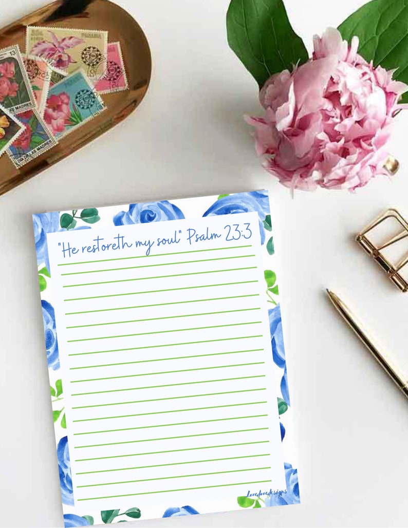 May include: A white lined notepad with a blue floral border and the text "He restoreth my soul" Psalm 23:3. The notepad has a green line pattern.