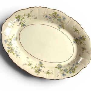 May include: Oval serving platter with a cream-colored base and a scalloped edge. The platter features a delicate floral pattern in blue and green, with a thin gold trim around the edge and the inner oval.