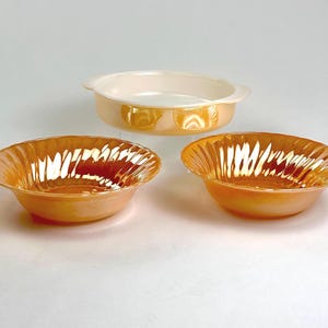 May include: Three vintage Pyrex bowls, two are peach colored with a swirl design and one is white with a round shape.