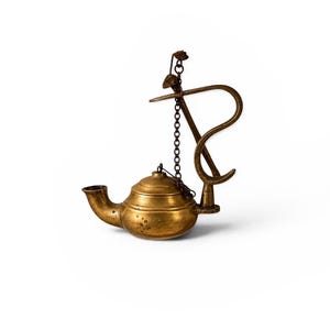 May include: A vintage-style brass oil lamp featuring a rounded body with a prominent spout, a domed lid, and a tall, curved handle. A thin metal chain connects the lid to the handle, which is topped with a small decorative metal leaf element.