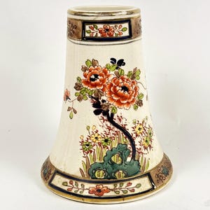 May include: Cream-colored ceramic vase with a flared shape, featuring floral designs in orange, green, and yellow. The vase has brown and blue decorative bands at the top and bottom, with a gold rim. The design includes a stylized tree and flowers.