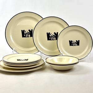 May include: Set of six cream-colored ceramic dinner plates with black trim and a silhouette design of two people sitting at a table. The plates are arranged in a staggered pattern on a white surface.
