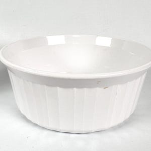 May include: A white ceramic baking dish with a fluted design. The dish is round and has a smooth, white interior.