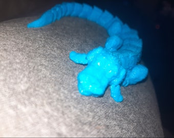 May include: A bright blue plastic alligator toy with a textured surface. The alligator is curled up in a playful pose.