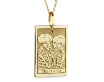 May include: A gold-toned rectangular pendant necklace featuring an engraved tarot card design. The pendant depicts two skeletons facing each other with a rose between them, the Roman numeral VI, and the text THE LOVERS at the bottom.