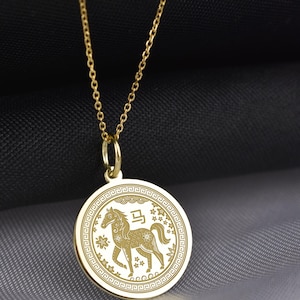 Peut inclure: Un collier pendentif circulaire dor&eacute; arborant un motif de cheval grav&eacute; au centre, accompagn&eacute; du caract&egrave;re chinois pour cheval, entour&eacute; d'une bordure g&eacute;om&eacute;trique d&eacute;corative et de petites &eacute;toiles, suspendu &agrave; une fine cha&icirc;ne dor&eacute;e.