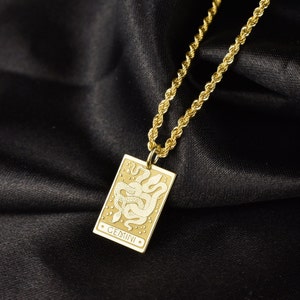 May include: Gold chain necklace with a gold pendant featuring a white outline of two snakes intertwined and the word "GEMINI" in white lettering.