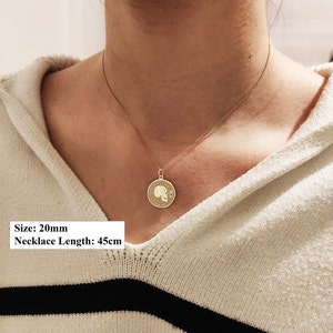 May include: A gold-toned circular pendant necklace featuring a skull engraving with hourglass symbols and the text MEMENTO MORI and AMOR FATI. The pendant measures 20mm in diameter and hangs on a chain with a total length of 45cm.