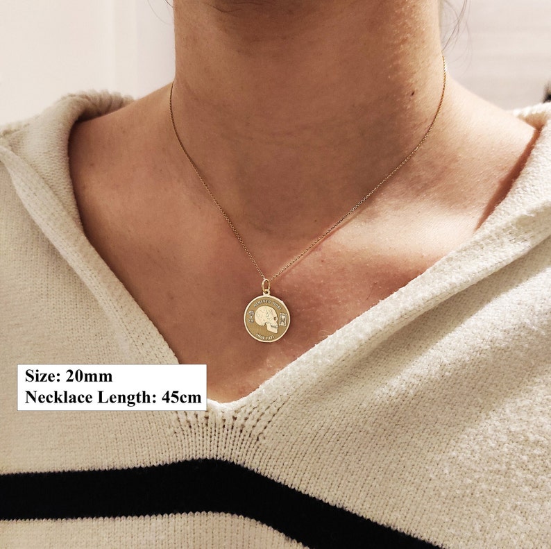 May include: A gold-toned circular pendant necklace featuring a skull engraving with hourglass symbols and the text MEMENTO MORI and AMOR FATI. The pendant measures 20mm in diameter and hangs on a chain with a total length of 45cm.
