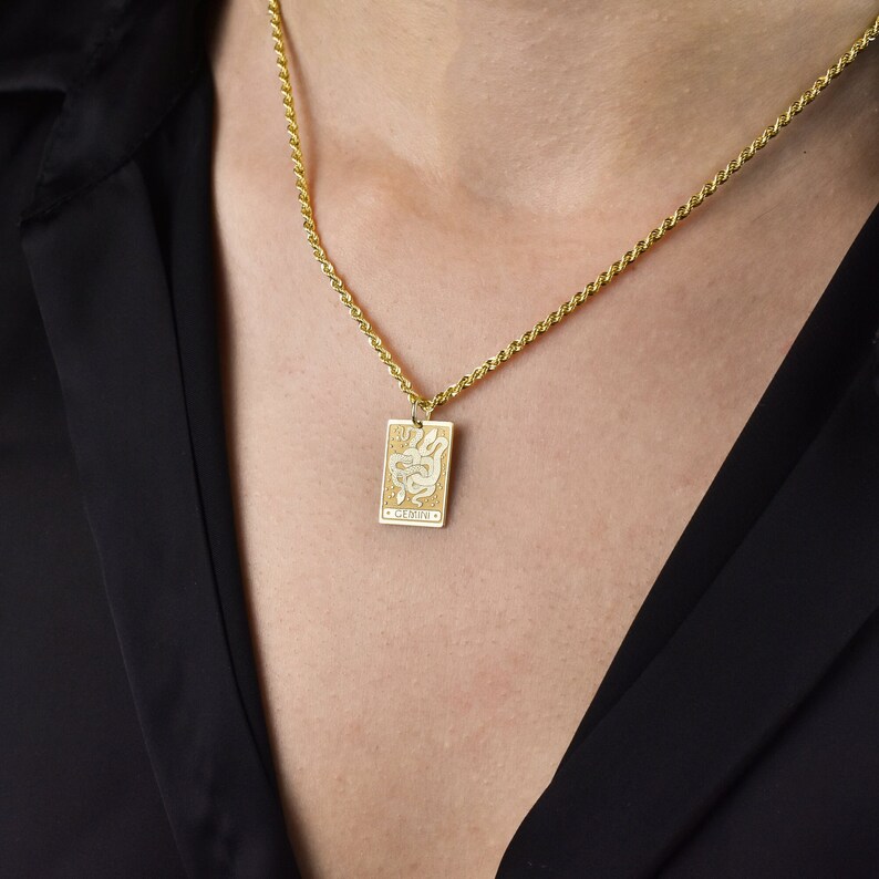May include: A gold chain necklace with a gold pendant featuring a white snake design and the word "Gemini" inscribed on it.