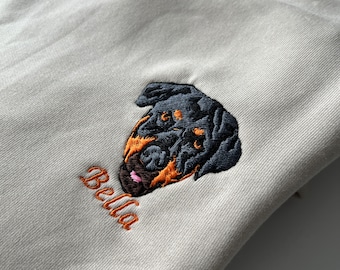 May include: Beige sweatshirt with an embroidered Rottweiler dog and the name "Bella" in orange thread.