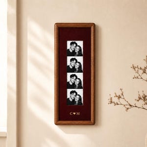 May include: A rectangular wooden photo frame with a dark red velvet matting. The frame holds a vertical strip of four black and white photographs featuring two people. The bottom of the matting displays the engraved letters C and M with a heart symbol.