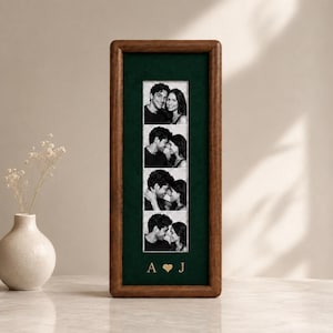 Peut inclure: Un cadre en bois rectangulaire vertical avec un passe-partout en velours vert foncé. Le cadre contient une bande de quatre photographies en noir et blanc d'un couple. Sous les photos, les lettres A et J dorées sont séparées par un petit cœur.