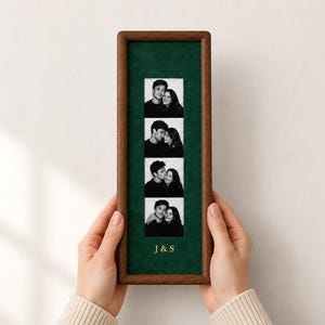 May include: A rectangular wooden frame with a dark green velvet matting containing a vertical strip of four black and white photographs of a couple. The letters J & S are printed in gold at the bottom of the green matting within the frame.