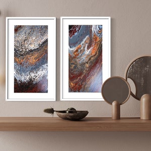 May include: Two framed abstract paintings with swirling patterns in shades of blue, brown, and orange, hanging on a beige wall above a wooden shelf with two decorative mirrors.