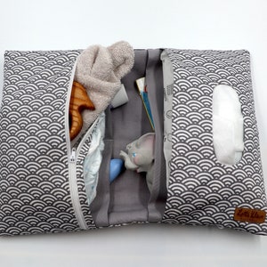 May include: A gray and white patterned baby changing pad with a zipper closure. The pad is open, revealing a diaper, toy, wipes, and other baby essentials. The pad has a gray interior and a white zipper.