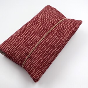 May include: A red fabric clutch with a subtle polka dot pattern and a brown leather flap closure.
