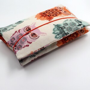 May include: A white fabric pouch with a colorful owl print. The pouch has a red ribbon closure.
