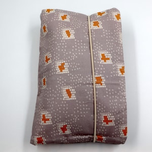 May include: A gray fabric pouch with a geometric pattern of orange and white squares. The pouch has a white elastic band running down the center.