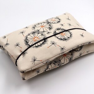 May include: A rectangular beige pouch with a black elastic band closure. The pouch is decorated with a repeating pattern of black and orange dandelion seed heads. The pouch is folded in half.