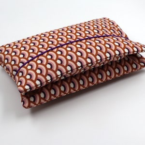 May include: A small, rectangular pouch with a brown, pink, and white geometric pattern. The pouch has a purple trim and is closed with a purple elastic band.