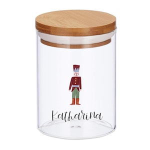 Può includere: Vaso di vetro trasparente con coperchio in legno. Il vaso presenta un'illustrazione ad acquerello di un soldatino con cappotto rosso e pantaloni verdi. Il nome "Katharina" è scritto in corsivo sotto.