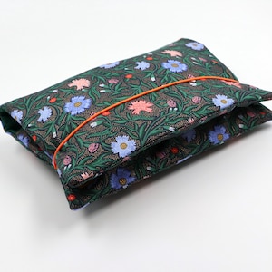 May include: A dark green fabric pouch with a floral print featuring pink, blue, and red flowers. The pouch is closed with a bright orange elastic band.