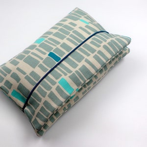 May include: A gray and white fabric pouch with a blue elastic band closure. The fabric has a geometric pattern of teal and blue rectangles.