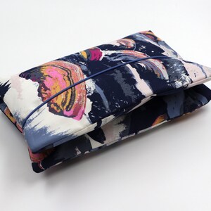 May include: A blue and white fabric pouch with a colorful abstract print. The pouch has a blue zipper and is folded closed.