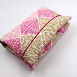 May include: A pink and gold geometric patterned fabric diaper clutch with a red elastic band closure.