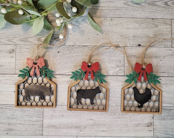 May include: Three wooden Christmas ornaments with a red bow and green leaves. Each ornament features a different farm animal silhouette: a pig, a cow, and a chicken. The ornaments are decorated with a brown and white chicken wire pattern.