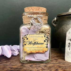 Può includere: Un barattolo da farmacia in vetro con tappo in sughero, spago e un ciondolo a forma di lupo argentato. Il barattolo contiene muschio essiccato, petali di lavanda e un'etichetta che recita "Wolfsbane". L'etichetta indica anche "Un ingrediente essenziale nelle pozioni per aiutare la trasformazione in lupo mannaro."