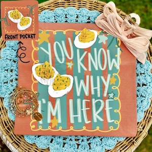 May include: A terracotta-colored shirt featuring a graphic of deviled eggs and the text "YOU KNOW WHY I'M HERE" in light blue. The design includes yellow stars and a scalloped border. A light pink fabric bow is attached to the top right corner.