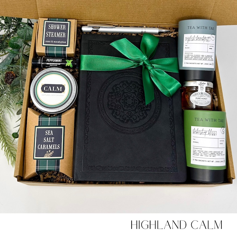 May include: A gift box with a black journal tied with a green ribbon, a pen, tea, honey, a shower steamer, lip balm, sea salt caramels, and a tin labeled "CALM." The box is labeled "HIGHLAND CALM."