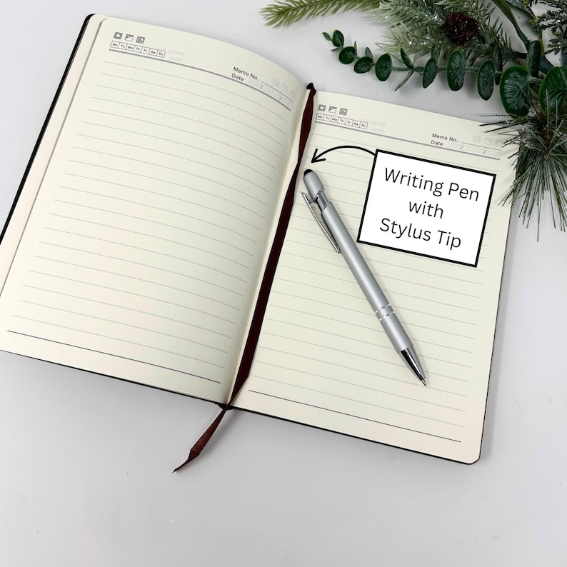 May include: An open, lined notebook with a silver writing pen with a stylus tip. The notebook has a black cover and a brown ribbon bookmark. The text "Writing Pen with Stylus Tip" is in a white box.