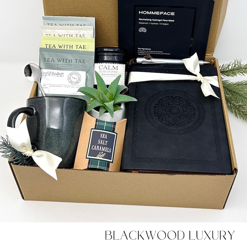 May include: A gift box filled with self-care items. Includes a mug, tea packets, a journal, a face mask, a small plant, sea salt caramels, and a pen. The box is labeled "BLACKWOOD LUXURY".