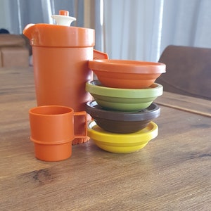 May include: A set of orange plastic kitchen play food, including a jug, a cup, and four nesting bowls in shades of orange, green, brown, and yellow.
