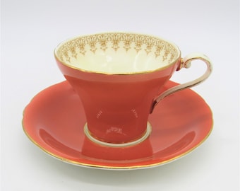May include: A coral-colored teacup and saucer set with a gold trim and a delicate floral pattern around the rim.