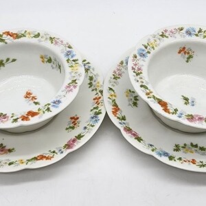 Könnte beinhalten: Zwei weiße Porzellanschalen mit Blumendesigns. Jede Schale hat einen gewellten Rand und steht auf einer passenden Untertasse. Die Schalen und Untertassen sind mit einem bunten Blumenmuster verziert.