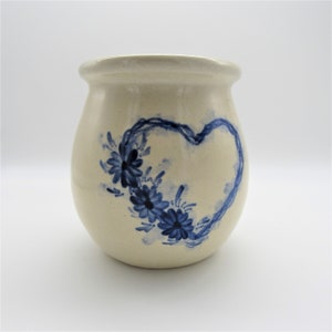 Könnte beinhalten: Eine cremefarbene Keramikvase mit einem blauen Herzdesign und blauen floralen Akzenten.