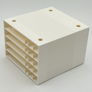 May include: A cream-colored, cube-shaped organizer with multiple horizontal slots. The organizer has a solid top with four evenly spaced circular holes. The side view reveals the layered structure, ideal for storing small items. The design is simple and functional.