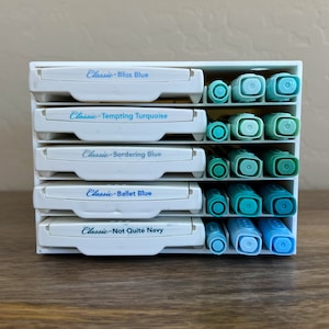 May include: A white plastic organizer with five rows of blue markers. Each row has a label with the name of a blue color: Bliss Blue, Tempting Turquoise, Bordering Blue, Ballet Blue, and Not Quite Navy.