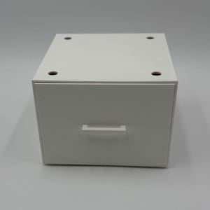 May include: A white, rectangular drawer with a simple, horizontal handle. The top of the drawer has four small, evenly spaced holes. The drawer is a solid, neutral color, and appears to be made of a smooth material.