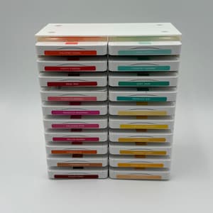 May include: A stack of ink pads in various colors, including red, pink, and teal. Each pad is labeled with its color name, such as "Calypso Coral" and "Poppy Parade". The ink pads are neatly arranged in two columns.