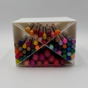 May include: A white, angled pen holder filled with a variety of colorful markers. The markers are arranged in rows, showcasing a spectrum of colors including orange, red, pink, purple, blue, and green. The pen holder is made of a solid white material.