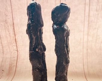 May include: Two black, tall, and slender candles with a rough, textured surface. The candles are standing upright on a light wood surface. The text "SHUN DESIGNS" is visible on a white label in the bottom center of the image.